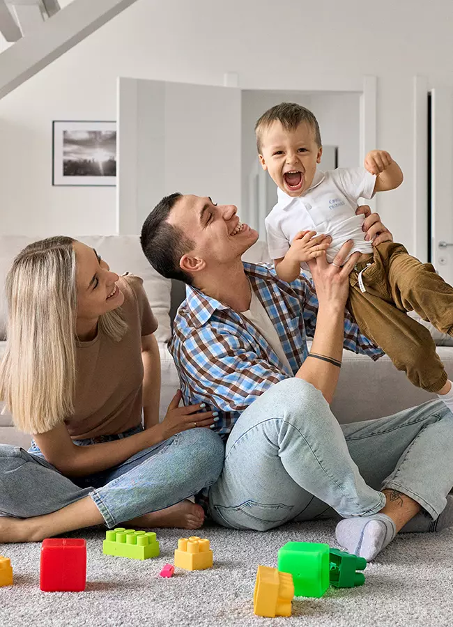 A joyful family playing with their child on the floor, laughing amid colorful toy blocks.