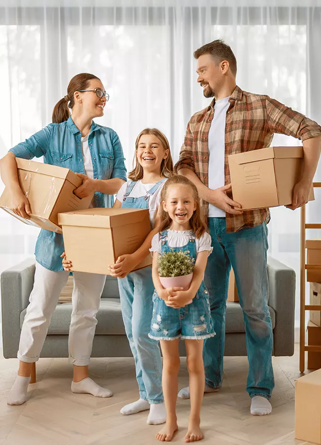 A joyful family carrying boxes and a plant, happily moving into their new home together.