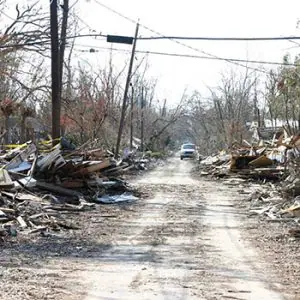 A deserted street with rubble lining the sides, leading to a car parked in the distance.